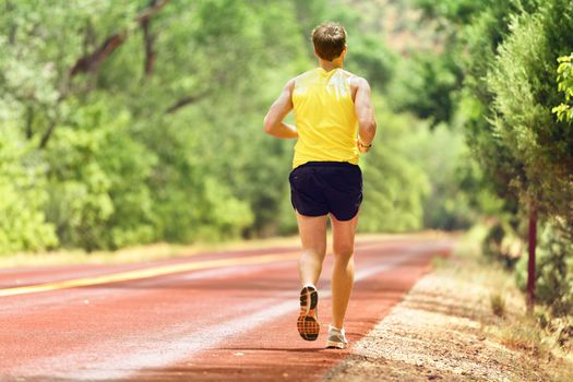 Running man runner working out for fitness. Male athlete on jogging run wearing sports running shoes and shorts working out for marathon. Full body length view showing back running away.