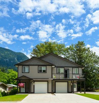 Modern residential duplex house with concrete driveway on mountain and cloudy sky background