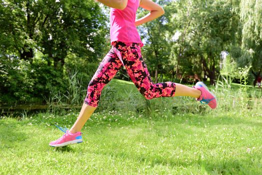 Female runner running shoes and legs in city park. Woman jogging wearing floral capris leggings compression tights and pink running shoes.