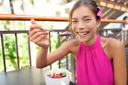 Acai bowl - woman eating healthy food smiling happy. Girl enjoy acai bowls made from acai berries and fruits outdoors for breakfast. Girl on Hawaii eating local Hawaiian dish.
