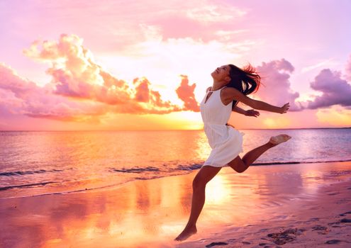 Happy beautiful free woman running on the beach at sunset jumping playful having fun in serene picturesque sunset at the ocean . Aspirational happy lifestyle with pretty young lady enjoying freedom.