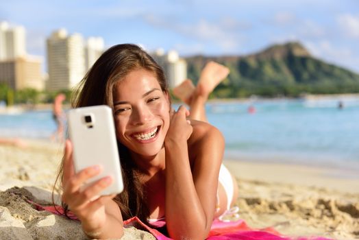 Smartphone woman using smart phone app on Waikiki Beach smiling laughing having fun. Girl sms text messaging or browsing on internet smiling happy outdoors. Mixed race Asian Caucasian on Oahu, Hawaii.