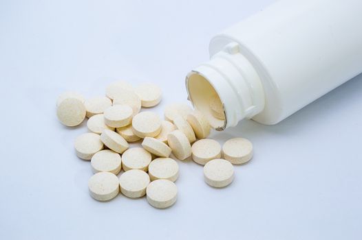 Vitamin tablets spilt from a white bottle and shown on a white background