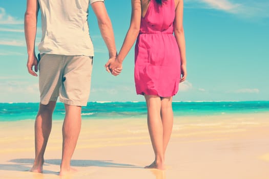 Low section of multiethnic couple holding hands on shore. Loving young tourists are standing at beach. They are spending leisure time together.