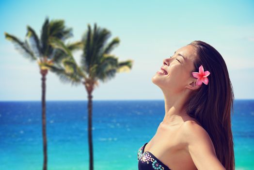 Happy young woman wearing flower while enjoying sunlight at beach. Mixed race Asian / Caucasian female is with eyes closed. She is on summer vacation.