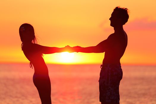 Silhouette couple holding hands at beach. Loving partners are spending quality time together during sunset. Side view of man and woman are enjoying their summer vacation.