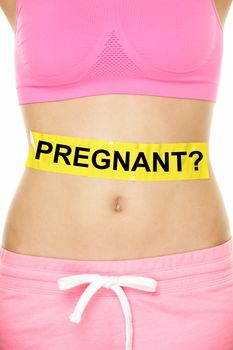 Midsection of young woman with pregnant written on yellow sign. Mixed race female is showing concept of doubt. She is standing against white background.