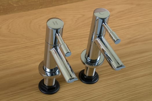 New chrome hot and cold taps ready to be fitted on a wooden background