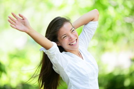 Joyful young woman raising arms in park. Attractive mixed race Asian / Caucasian female is in casuals. She is looking away while smiling.