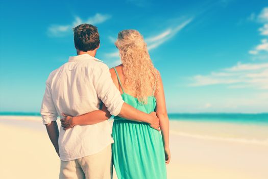 Rear view of young Caucasian couple with arms around. Loving partners are standing at shore. Man and woman are enjoying summer vacation at beach.