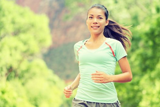 Young woman jogging while smiling. Beautiful mixed race Asian / Caucasian female is in sports clothing. Attractive lady is in park.