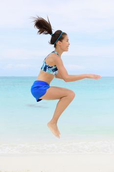 Crossfit fitness Asian woman on beach doing jump squat plyometric training exercises by jumping and touching knees as part of a full body core workout and active lifestyle.