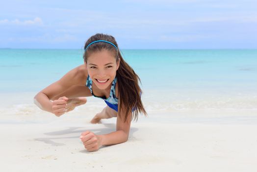 Core body workout - fitness woman planking doing forearm one arm spiderman knee to elbow crunch plank. Young Asian Chinese adult girl on beach strength training as part of a healthy lifestyle.