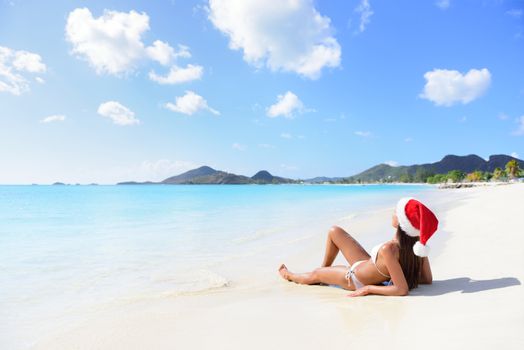 Christmas beach woman wearing santa hat and bikini on holidays travel vacation getaway travel relaxing on tropical beach lying in the sand. Beautiful young female model.