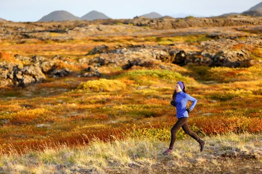 Woman trail runner running in mountain landscape. Female runner in warm winter and fall outfit jogging cross country outdoors in beautiful nature.