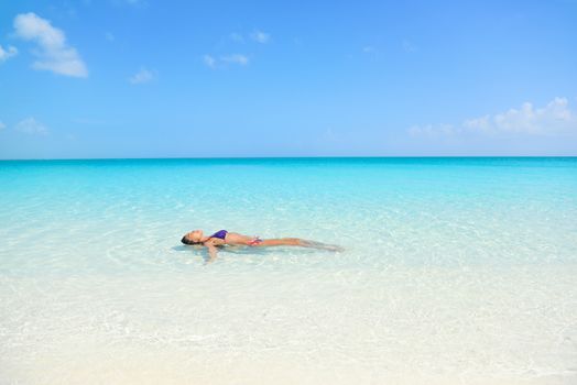 Woman swimming in ocean relaxing enjoying the sun bathing in peaceful blue water. Sexy female adult floating meditating in the sea.