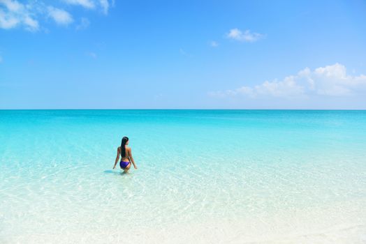 Beach holiday person swimming in blue ocean. Sexy bikini woman relaxing enjoying her tropical vacation in the Caribbean in a paradise destination with perfect turquoise water and white sand.