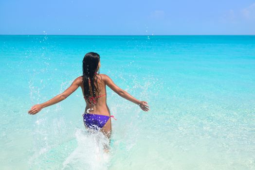 Beach vacation in tropical travel destination. Sexy woman in bikini feeling free swimming splashing water in blue ocean enjoying her sunny holidays. Concept of people having fun under the sun.