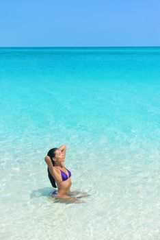 Beach woman in bikini swimming in blue ocean. Beautiful Asian girl sun tanning and relaxing in water taking care of her hair and skin.