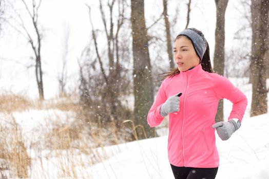 Winter jogging - young Asian Chinese adult woman runner running breathing cold air wearing pink windbreaker jacket, headband and gloves doing a cardio workout.