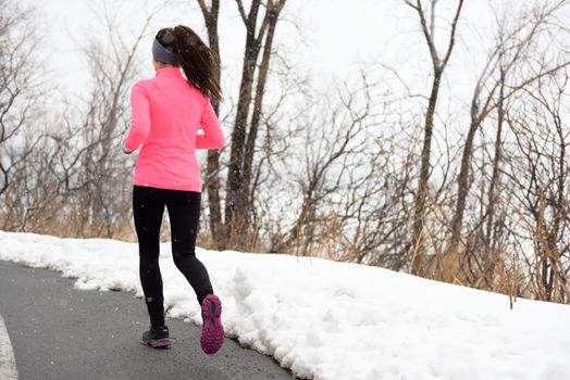 Winter jogging in park - female runner from the back exercising her cardio wearing pink jacket, active leggings and running shoes on city path.