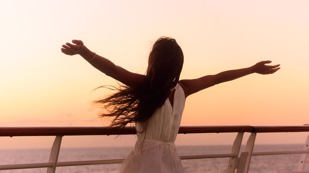 Cruise ship vacation woman enjoying sunset on travel at sea. Free happy woman looking at ocean in happy freedom pose with arms out. Woman in dress on luxury cruise liner boat.