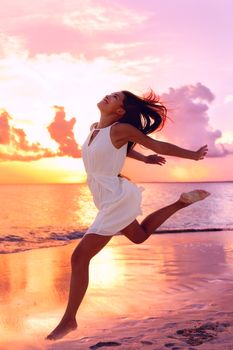 Carefree woman jumping at beach during sunset. Full length of female is wearing sundress. Tourist is enjoying vacation against orange sky at sea shore.