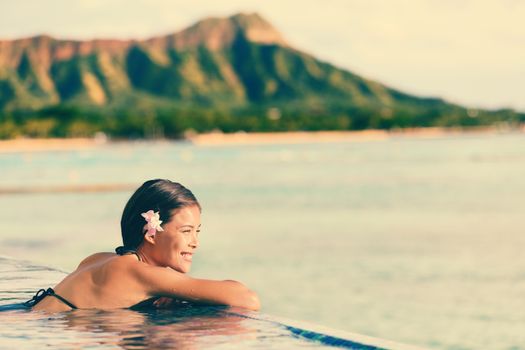 Smiling beautiful woman relaxing in infinity swimming pool. Side view of happy female looking at ocean view on sunny day. Young tourist is enjoying summer vacation against mountain.