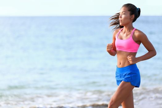 Determined woman jogging on beach. Fit young female is in sports clothing. Jogger is exercising against ocean during sunny day.
