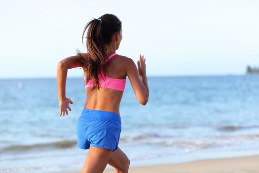Fit young woman jogging on beach against sky. Rear view of determined female is in sports clothing. Runner is exercising at sea shore during sunny day.