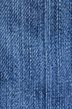 Jeans fabric background. Worn jean pants closeup of faded blue denim weave texture with vertical weave lines useful for elements of illustration, text copyspace or backgrounds.
