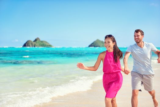 Happy multiracial Asian Caucasian couple having fun walking on perfect turquoise Lanikai Hawaii beach for summer vacation on Hawaiian island, Oahu, USA.