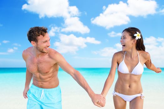 Beach vacation fun sexy couple in bikini swimwear and blue swim shorts on perfect turquoise ocean background. Happy people holding hands laughing with slim shape. Weight loss suntan body care concept.