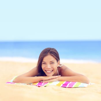 Happy vacation woman sunbathing relaxing on beach. Cute young Asian Caucasian ethnic mixed race girl lying down tanning under the sun on pastel towel on golden sand.