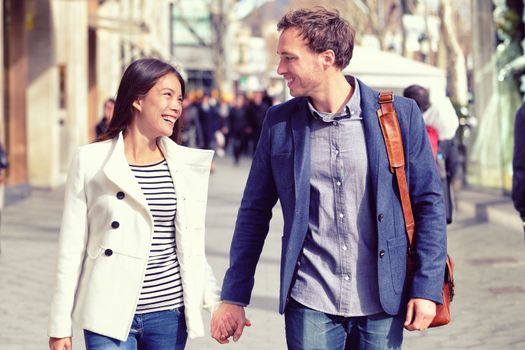 Young dating couple in love walking in city. Business people or office colleagues flirting after work holding hands on street in fall, spring or winter wearing smart casual blazer jacket and suit.