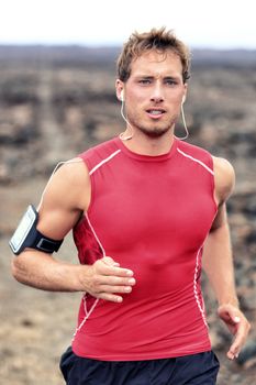 Trail runner man working out wearing earphones listening to smartphone music playlist. Male athlete on mountain path training cardio with armband mobile phone holder. Tech fitness gear concept.