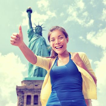 Happy Asian Chinese tourist doing thumbs up having fun visiting the Statue of Liberty, american landmark in New York City. Famous touristic attraction, USA.