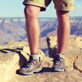 Outdoor hiking shoes - closeup crop of legs of male hiker walking in wool socks and boots on summer nature trail, grand canyon background. Active lifestyle adventure gear concept.