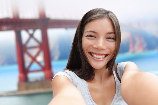 Selfie girl on San Francisco Golden bridge travel. Cute young Asian woman adult taking picture with her smartphone during summer vacation in front of the famous American attraction, California, USA.