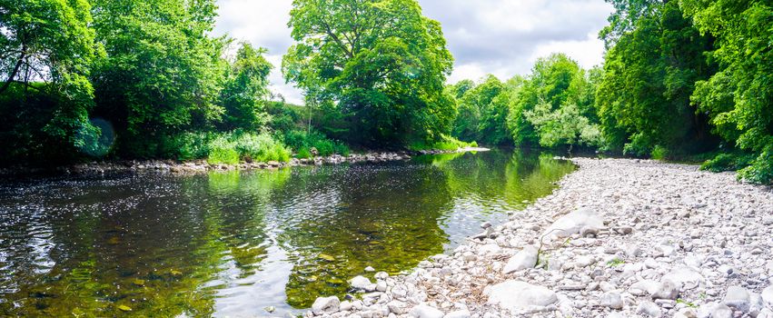 River Kent running over the rocks and pebbles with tree lined banks in summer