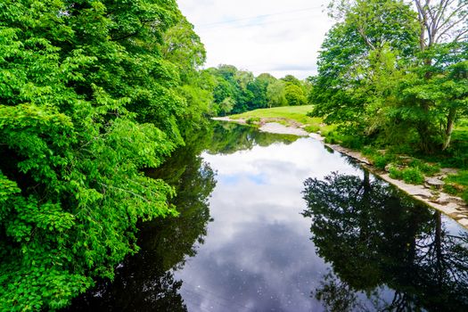 standing on a bridge looking down a slow moving river with green banks