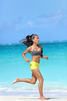 Active, healthy and fit lifestyle - woman running barefoot on beach. Asian female runner jogging full length on sand training her leg muscles and cardio on ocean background.
