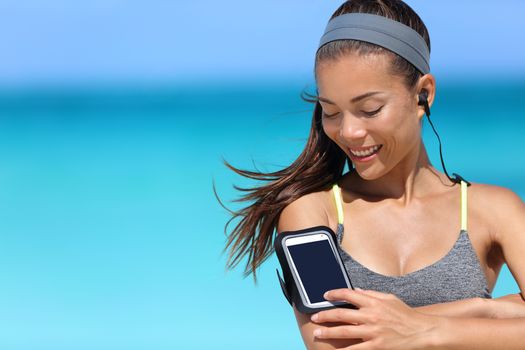 Fit woman using smartphone fitness app on armband. Young Asian female runner touching the display touchscreen on sports arm strap with mobile phone for listening to music or as activity tracker.