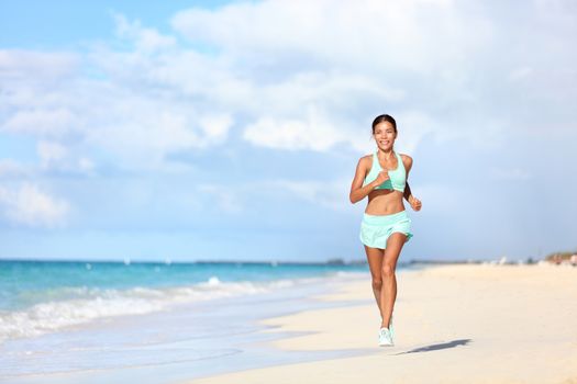 Happy fit female runner running on sand during summer travel vacation on tropical beach. Asian woman jogging doing cardio training exercising for weight loss. Happiness and wellbeing concepts.