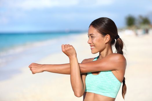 Athlete runner doing fitness warm-up before strength training stretching shoulder and arms. Sporty Asian woman preparing for workout and run doing body and arm muscle stretches happy on beach.