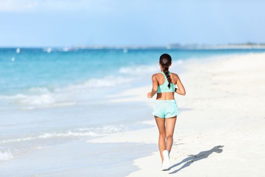 Sporty runner in running outfit training cardio jogging on sunny beach. Unrecognizable person exercising legs and body on white sand next to ocean waves.