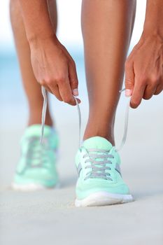 Sportswoman runner getting ready tying running shoes on beach. Fitness woman living a healthy and active life preparing for cardio training. Wellness and health concept.