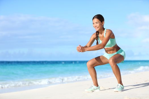 Fitness young woman working out core and glutes with bodyweight workout doing squat exercises on beach. Asian sporty girl squatting legs as part of an active and fit life.