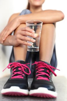 Fitness athlete woman drinking water holding glass - hand closeup hydration concept. Runner woman preventing dehydration for her health and body.