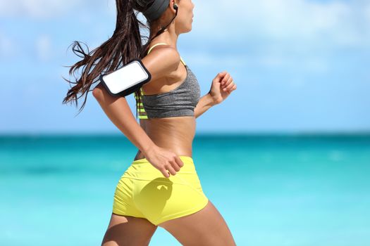 Sports phone armband fitness jogger exercising on beach - cardio workout. Midsection closeup of female athlete runner jogging wearing smartphone sleeve and earphones. Glutes training.